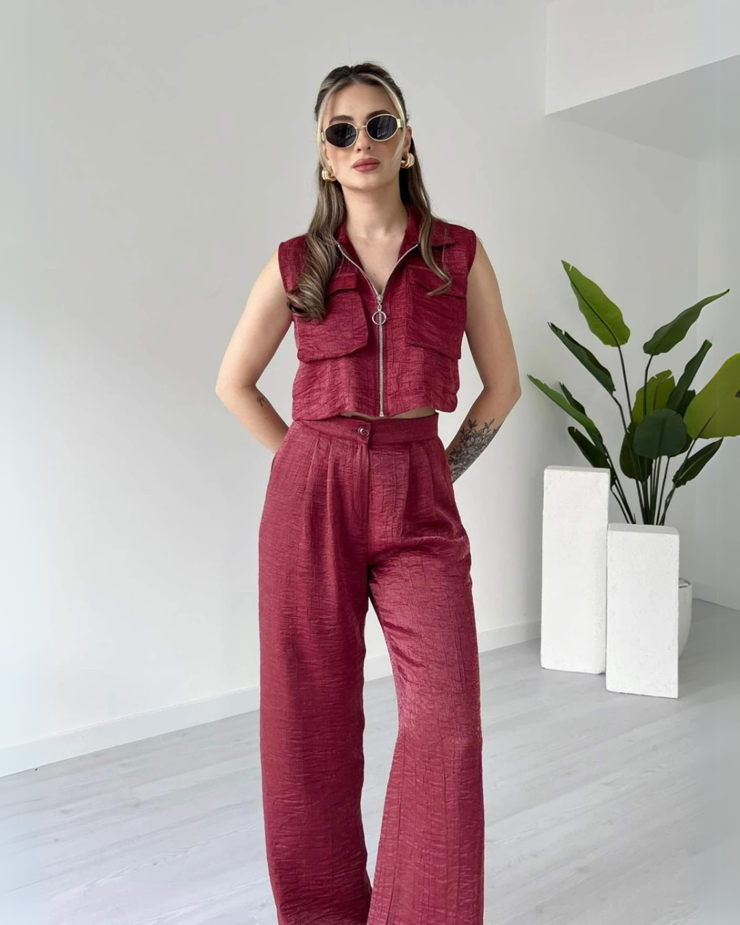 Woman wearing a stylish sleeveless maroon co-ord set with zip-up crop top and high-waisted wide-leg pants – minimal indoor fashion shoot